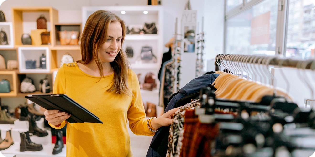 Woman walking down aisle in retail clothing store while holding a notebook